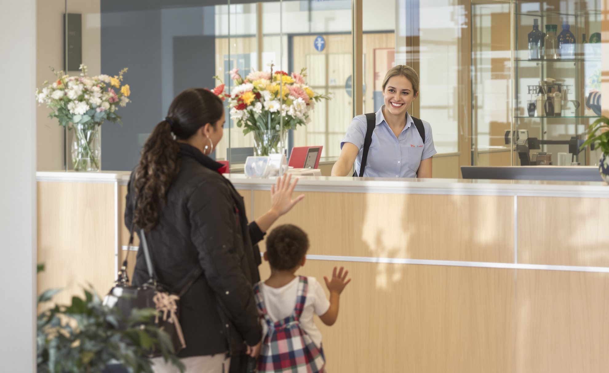 A smiling front office staff member greeting a parent and child at a school welcome desk