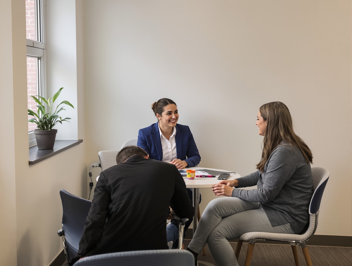 A counsellor and a teacher sitting with a student at a small table in a bright office.