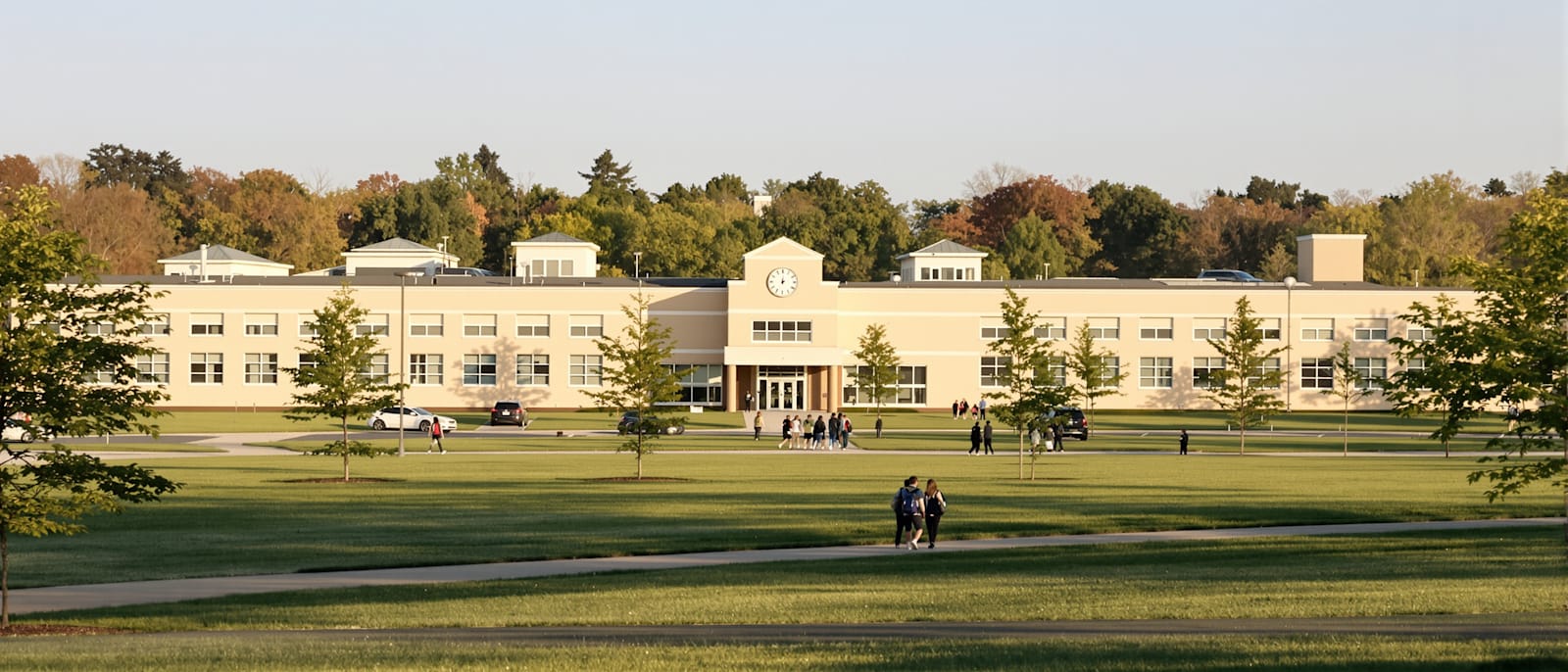 A low suburban school building with students walking across the lawn toward the entrance on a sunny morning.