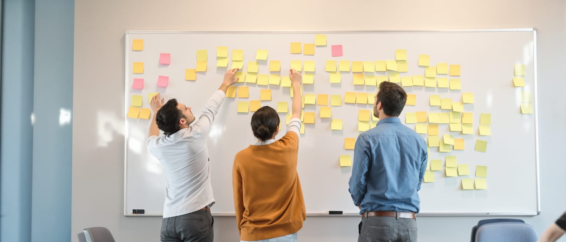 Two colleagues working through options at a whiteboard covered in blank sticky notes.