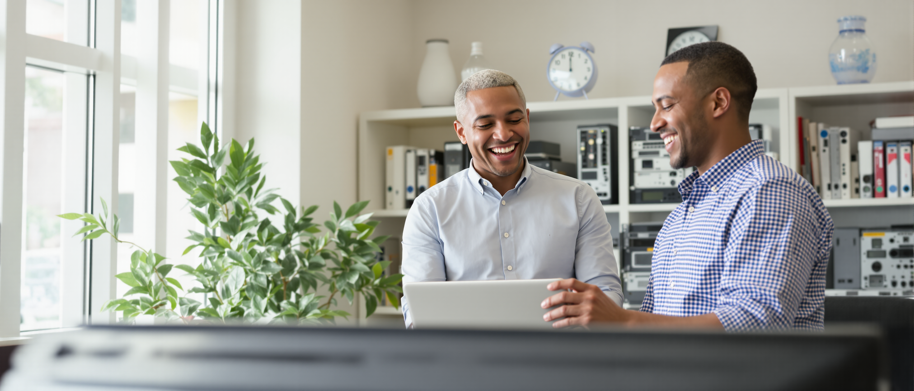 Two IT staff members smiling while reviewing a laptop together in an office